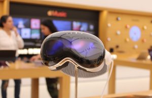 Apple Unveils Vision Pro Head-Worn Computer A person wearing the Apple Vision Pro headset gestures in the air while digital windows float in their surroundings.