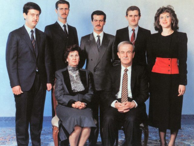 Assad family Bashar al-Assad speaking at a podium with Syrian flags in background