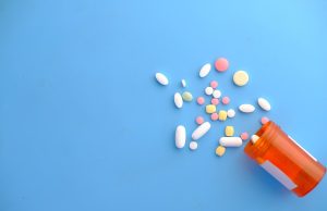 Migraine Drug Class Elevated to Standard Treatment A person holding a small white pill bottle with a migraine headache graphic in the background