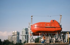 RESQSHIP Saves 59 from Coffin Dinghy, 3 Children Die Overcrowded gray inflatable dinghy adrift on open sea as orange rescue vessel approaches