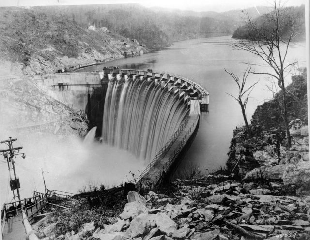 Tennessee Dam Failure Report Proven False After Evacuation Order Issued Concrete arch of Walters Dam spanning the Pigeon River in the Great Smoky Mountains with autumn foliage on the banks.