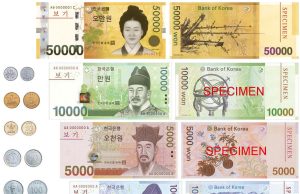 South Korean Won Plunges to Two-Year Low After Martial Law South Korean won banknotes and coins arranged on a table, with a stock market chart showing a sharp decline in the background.