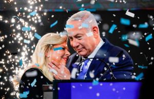 Netanyahu Wins Landslide Likud Primary Victory Benjamin Netanyahu speaks at a campaign event, surrounded by Likud party supporters holding blue and white flags.