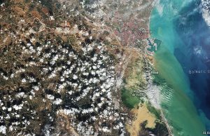 Spain Floods Kill Hundreds in Valencia, Andalusia Regions Murky brown floodwater surges through a Spanish town street, half-submerging cars and ground-floor shops under a still-grey sky.